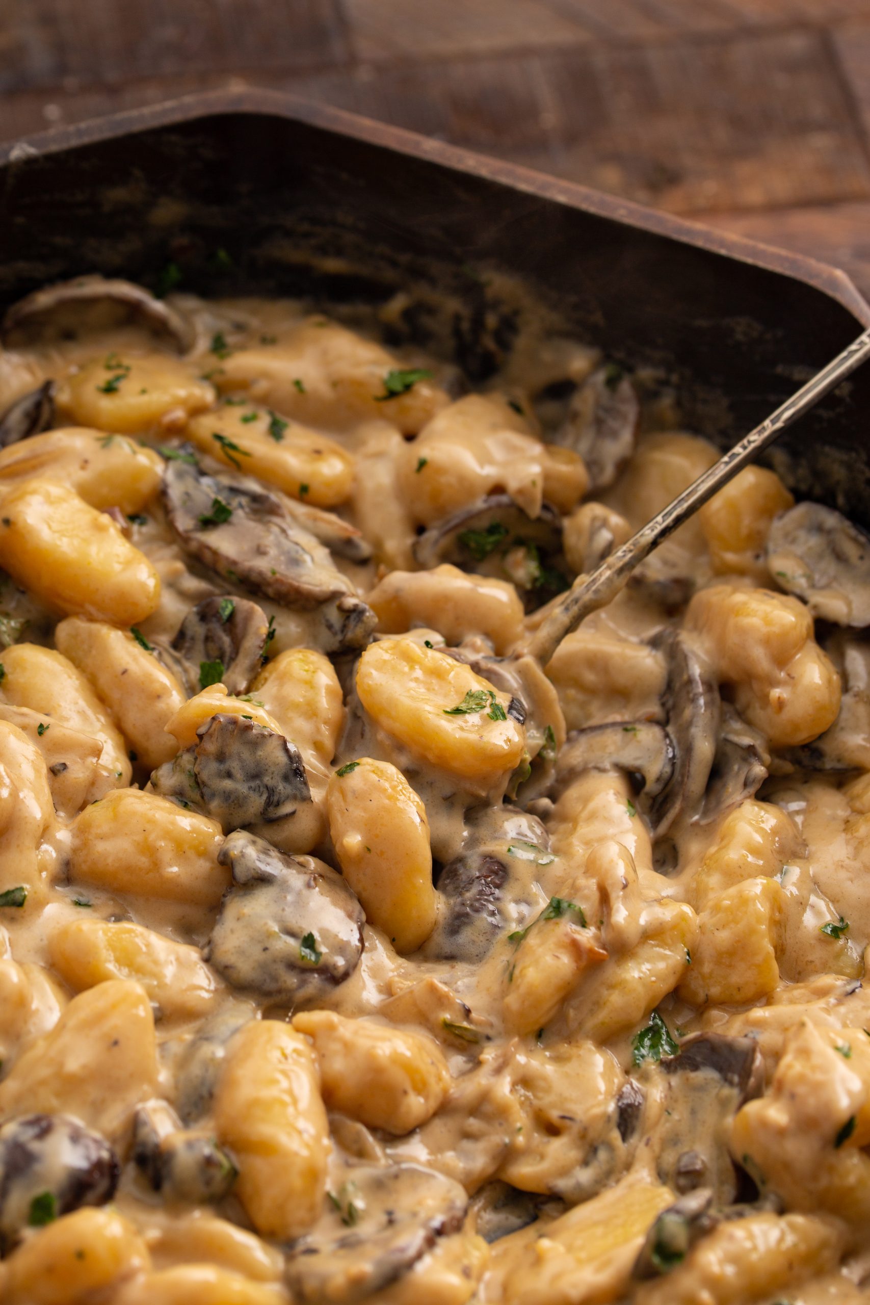 A pan of creamy gnocchi mixed with mushrooms and garnished with herbs.