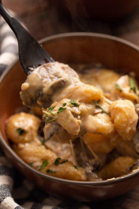 A close-up of pasta in a creamy sauce on a fork, garnished with herbs.