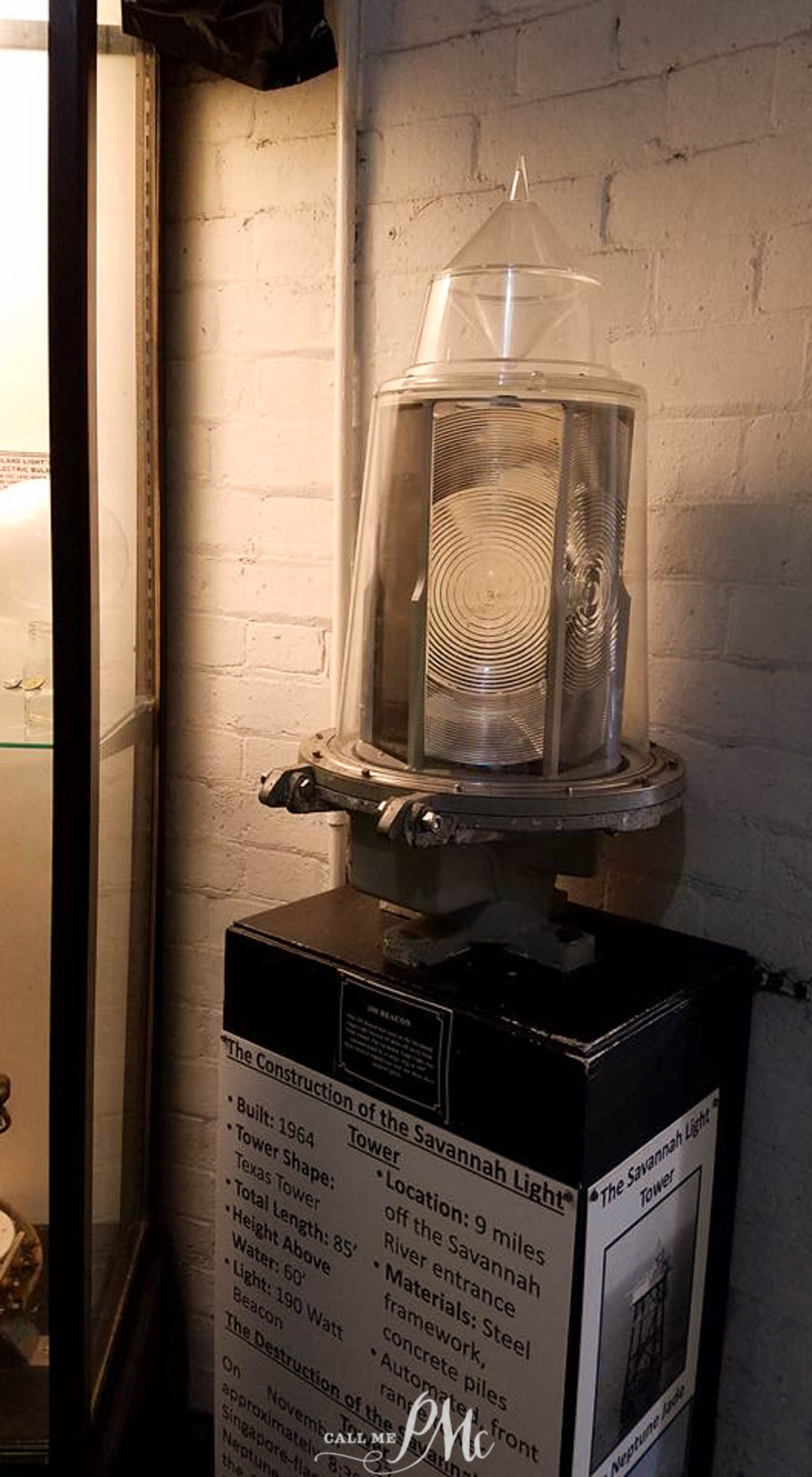 48 hours in Savannah. A lighthouse lens displayed in a museum with informational text about the construction of the Savannah Light Tower. The lens is encased in glass and mounted on a black pedestal.