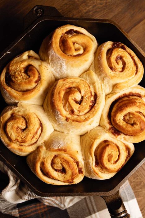 A cast iron skillet filled with freshly baked cinnamon rolls resting on a wooden surface.