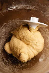 A ball of dough being mixed in a stand mixer's bowl.