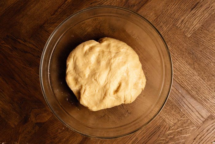 A ball of dough resting in a clear glass bowl on a wooden surface.