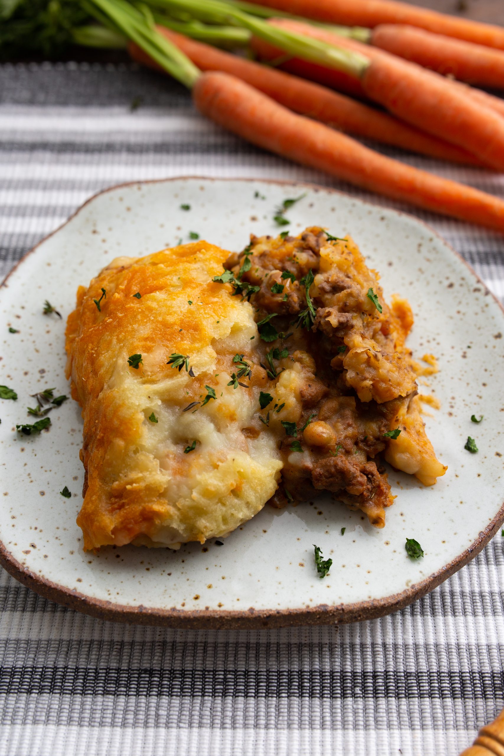 Close-up of a fork holding a bite of shepherd's pie with visible meat, vegetables, and mashed potatoes, garnished with parsley.