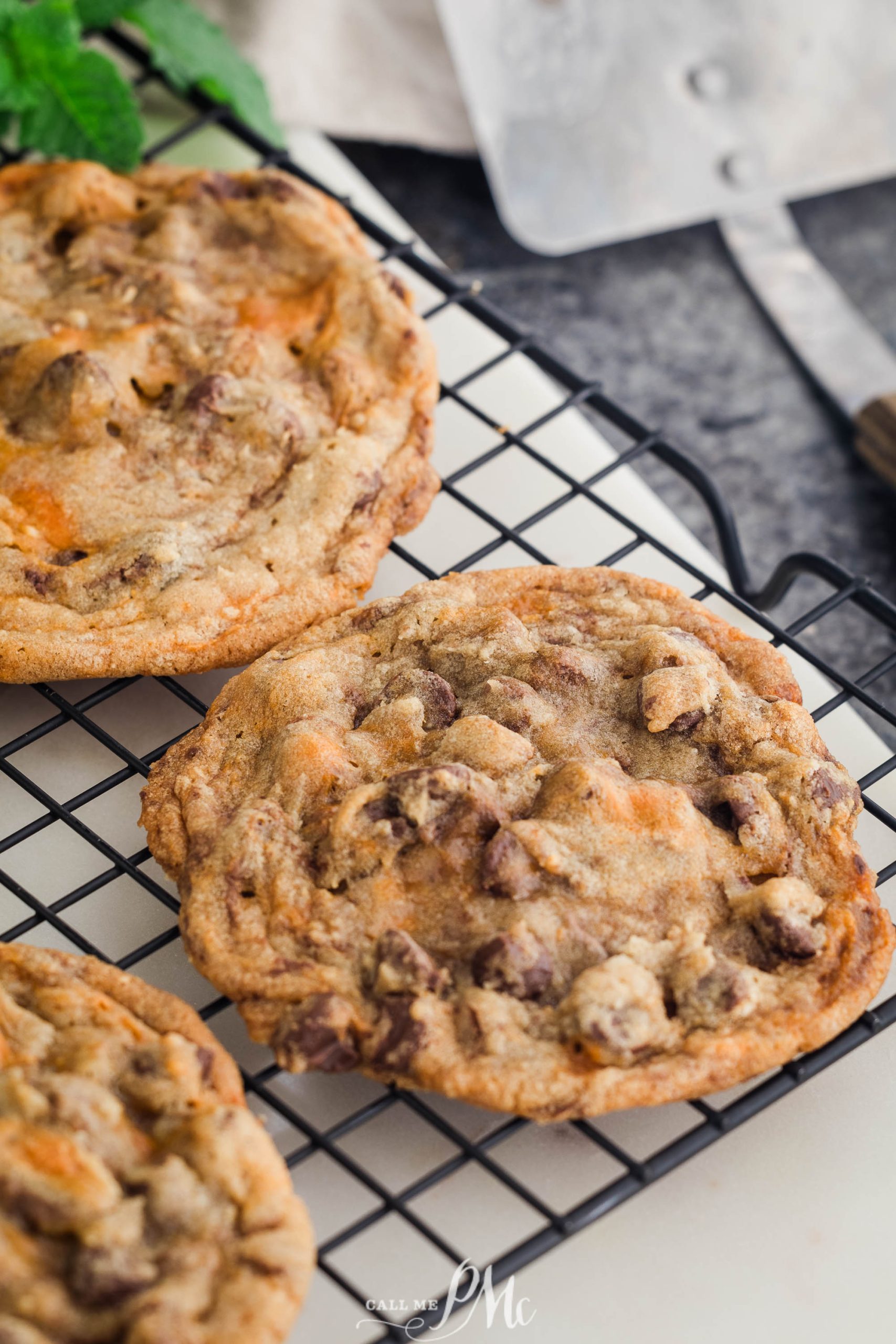 Three freshly baked chocolate chip cookies cooling on a black wire rack.