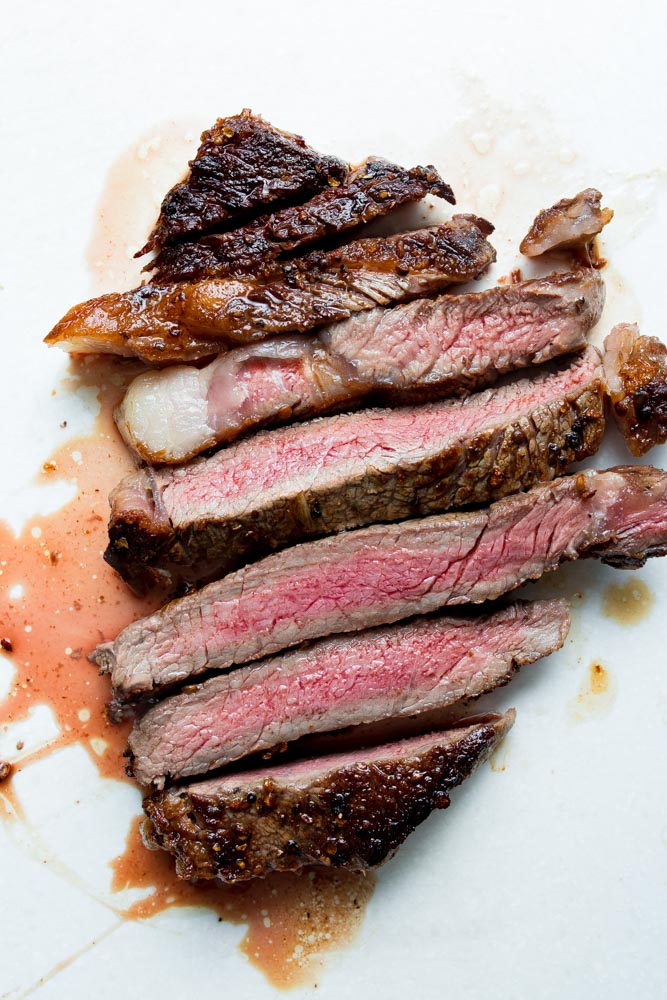 Slices of medium-rare steak with seared edges and some juice on a white surface.