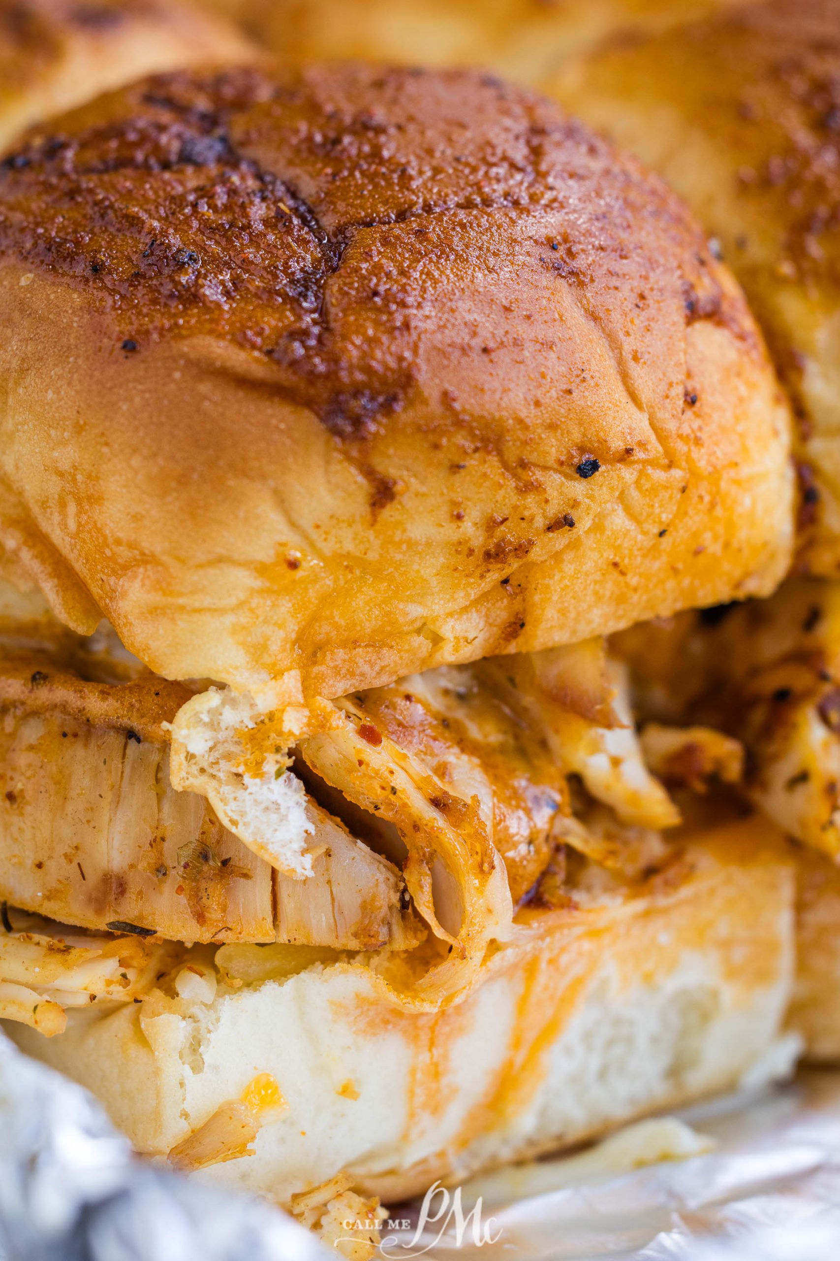 Close-up of a barbecue chicken sandwich on a bun with visible seasoning. The sandwich is partially wrapped in foil.