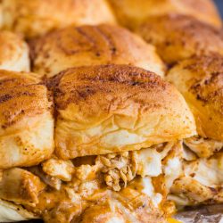 Close-up of several seasoned chicken sliders with melted cheese on soft buns, placed on aluminum foil.