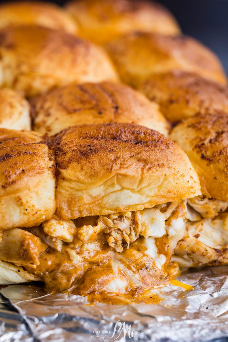 Close-up of several seasoned chicken sliders with melted cheese on soft buns, placed on aluminum foil.