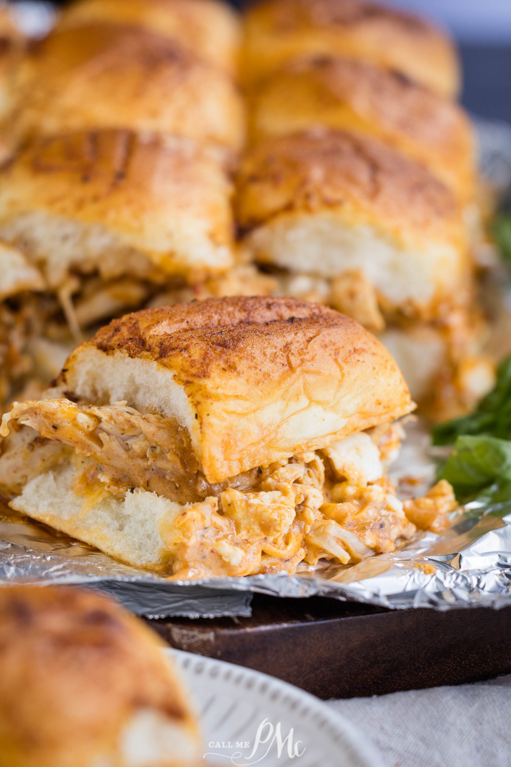 A close-up shot of several sliders filled with shredded chicken and melted cheese placed on aluminum foil.