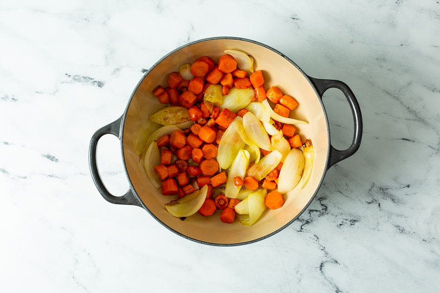 A black pot on a marble surface contains cooked pieces of carrots and onions.