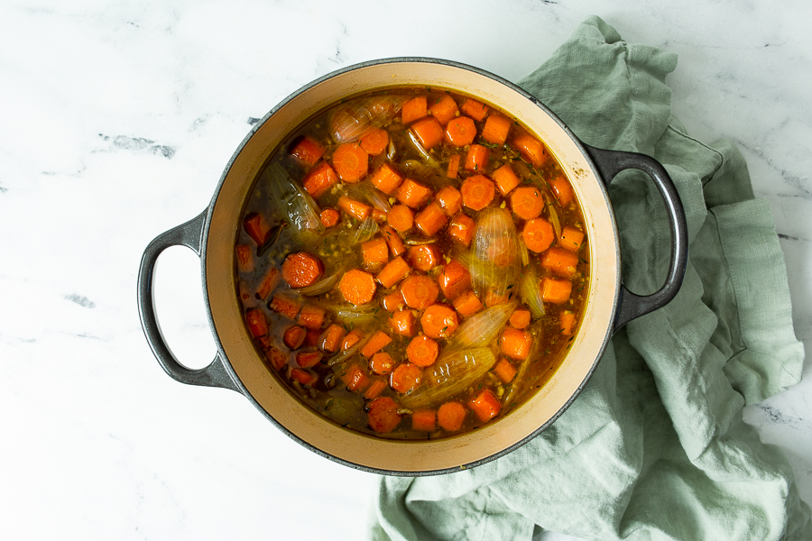 A pot filled with a carrot stew containing chopped carrots and onions, placed on a green cloth on a marble countertop.