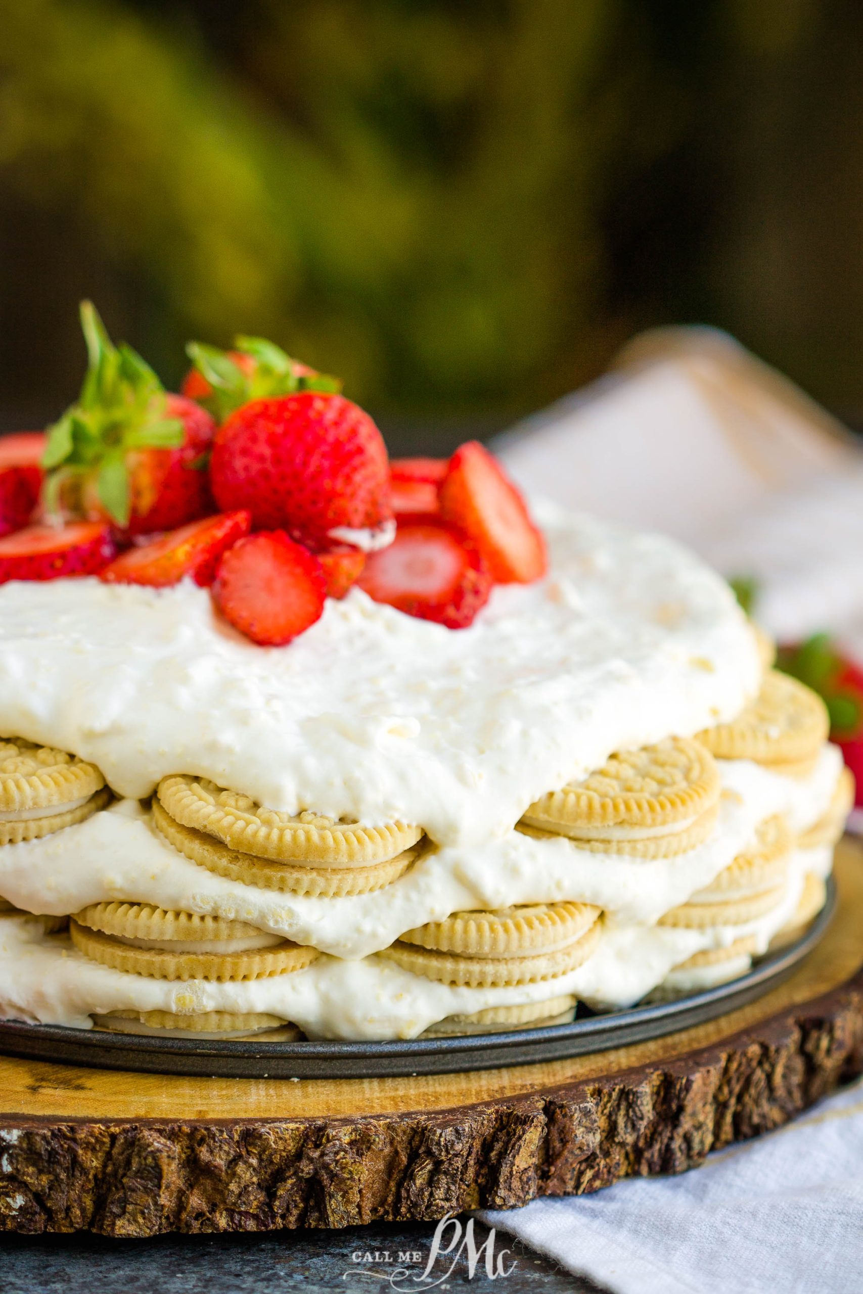 A layered key lime icebox cake dessert made with golden sandwich cookies, creamy white filling, and topped with fresh strawberries on a rustic wooden board.