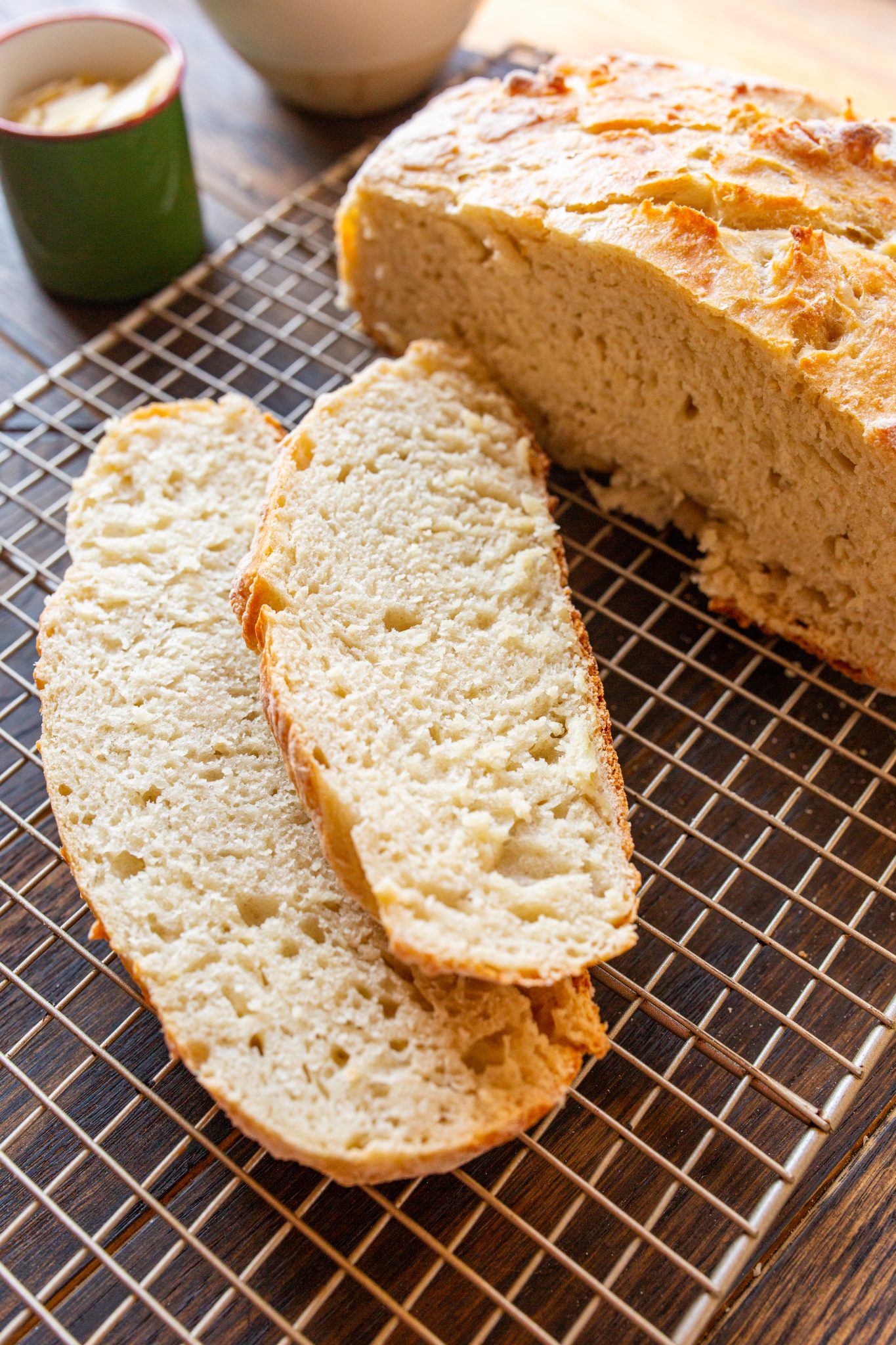 A loaf of sliced Dutch Oven No Knead Bread is placed on a wire cooling rack with two pieces in the foreground.