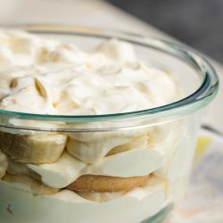 A glass dish filled with layers of banana pudding, sliced bananas, and creamy topping.