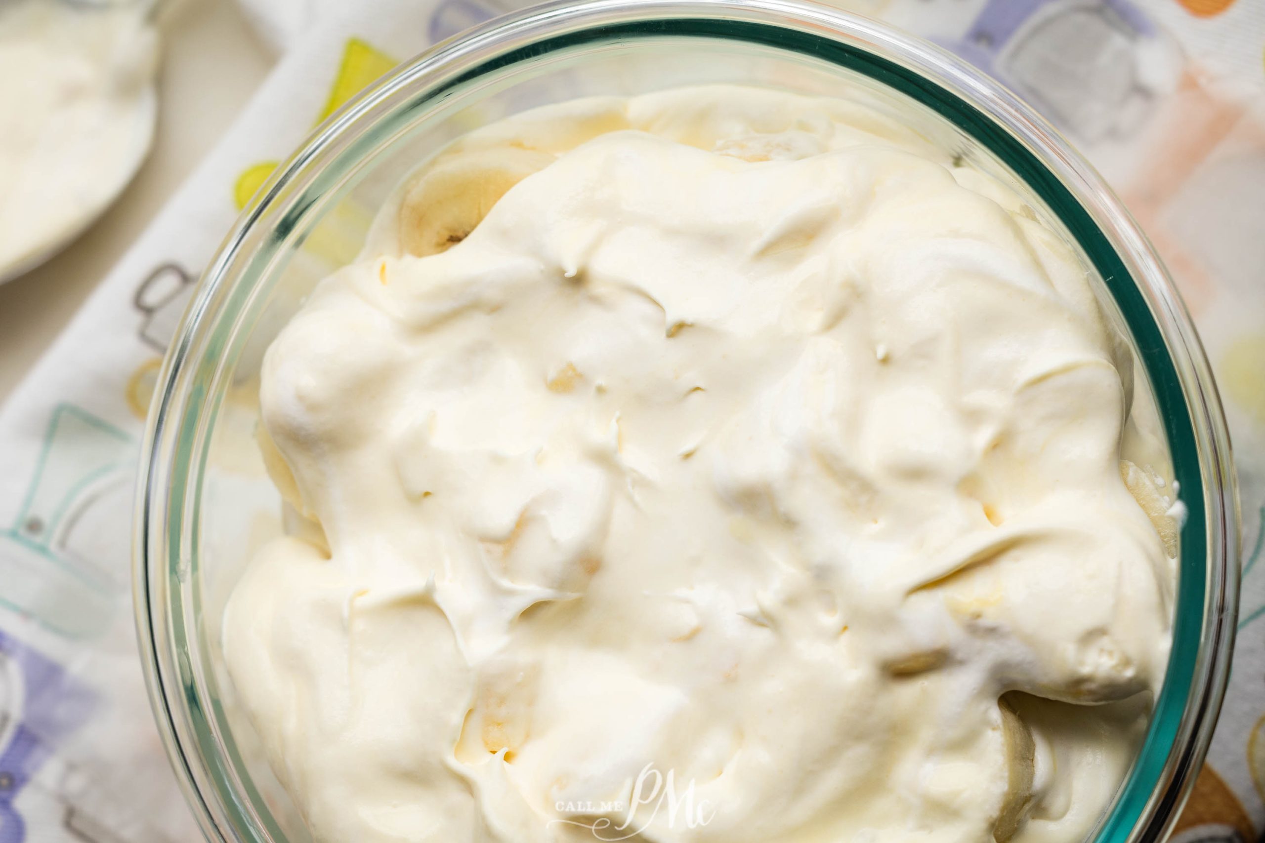 A glass bowl filled with a creamy, white dessert sits on a patterned cloth.