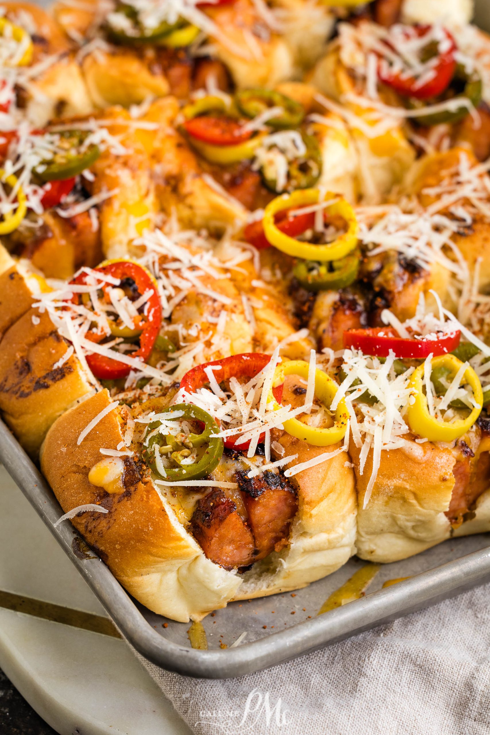 Tray of baked sliders topped with shredded cheese, jalapeno slices, and red bell pepper rings.