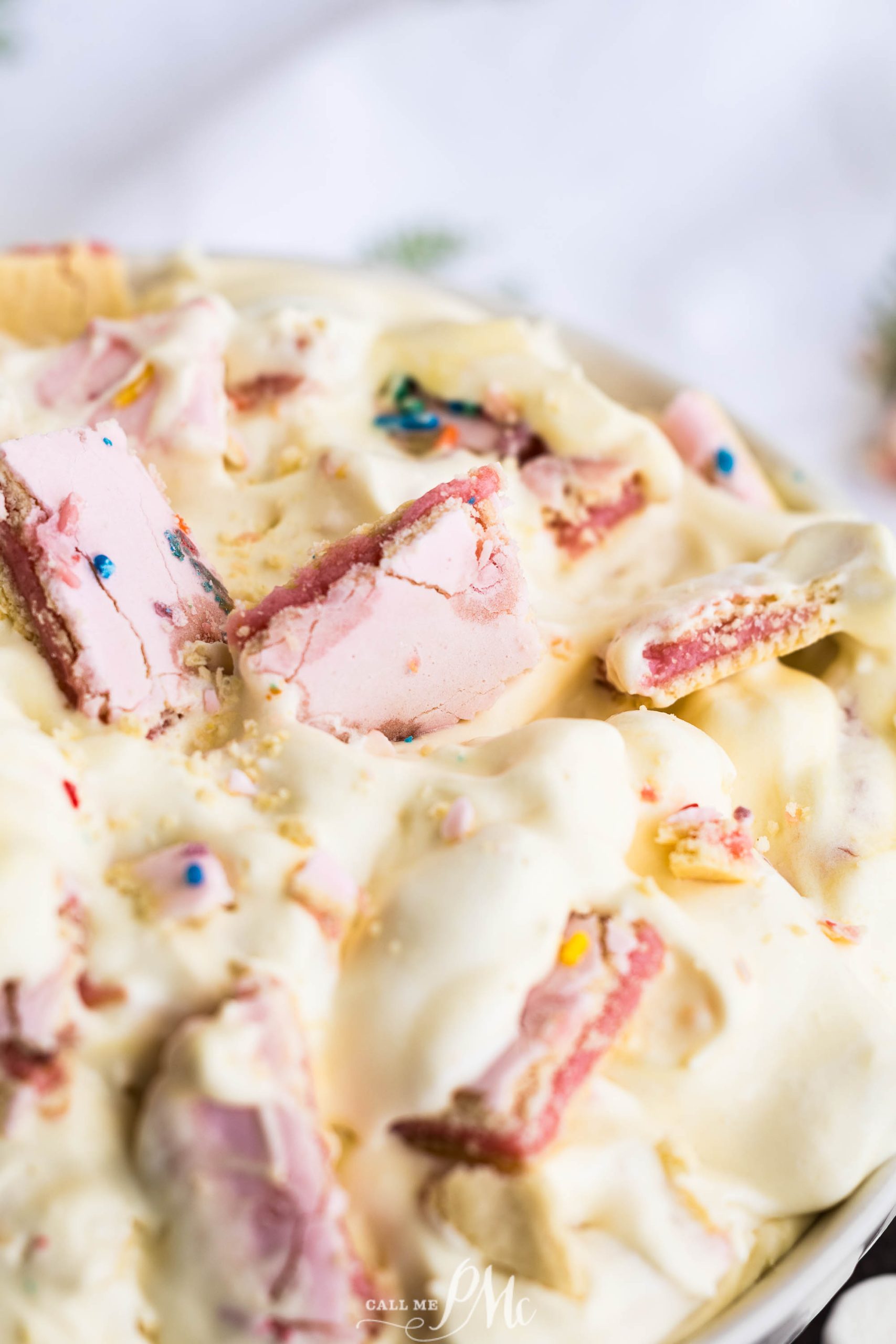 A close-up image of a creamy dessert topped with chunks of a pink sweet treat and colorful sprinkles.