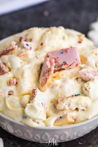 A bowl of creamy dessert with chunks of pink candy and rainbow sprinkles mixed in.