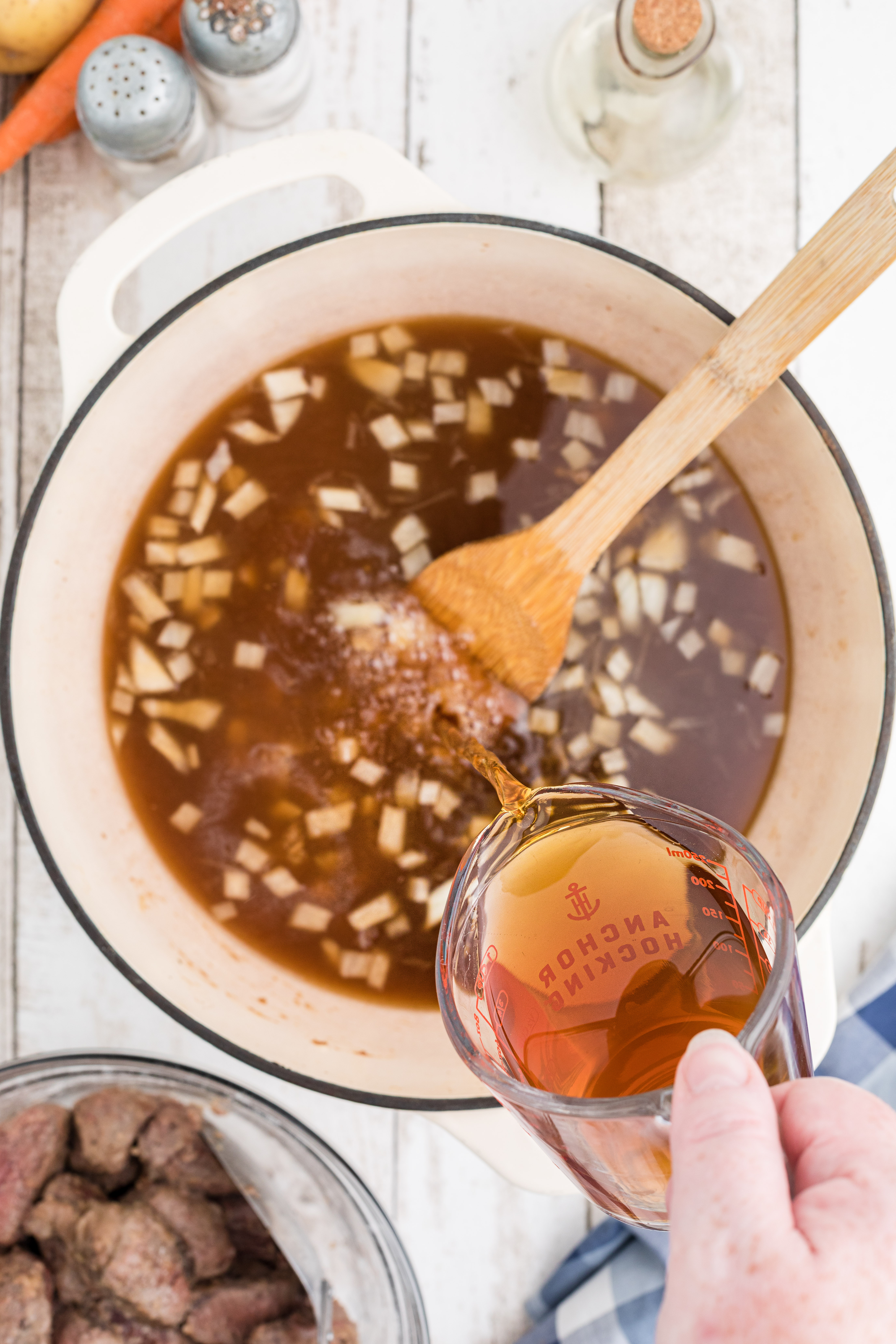 Beef broth being poured into the pot with onions.