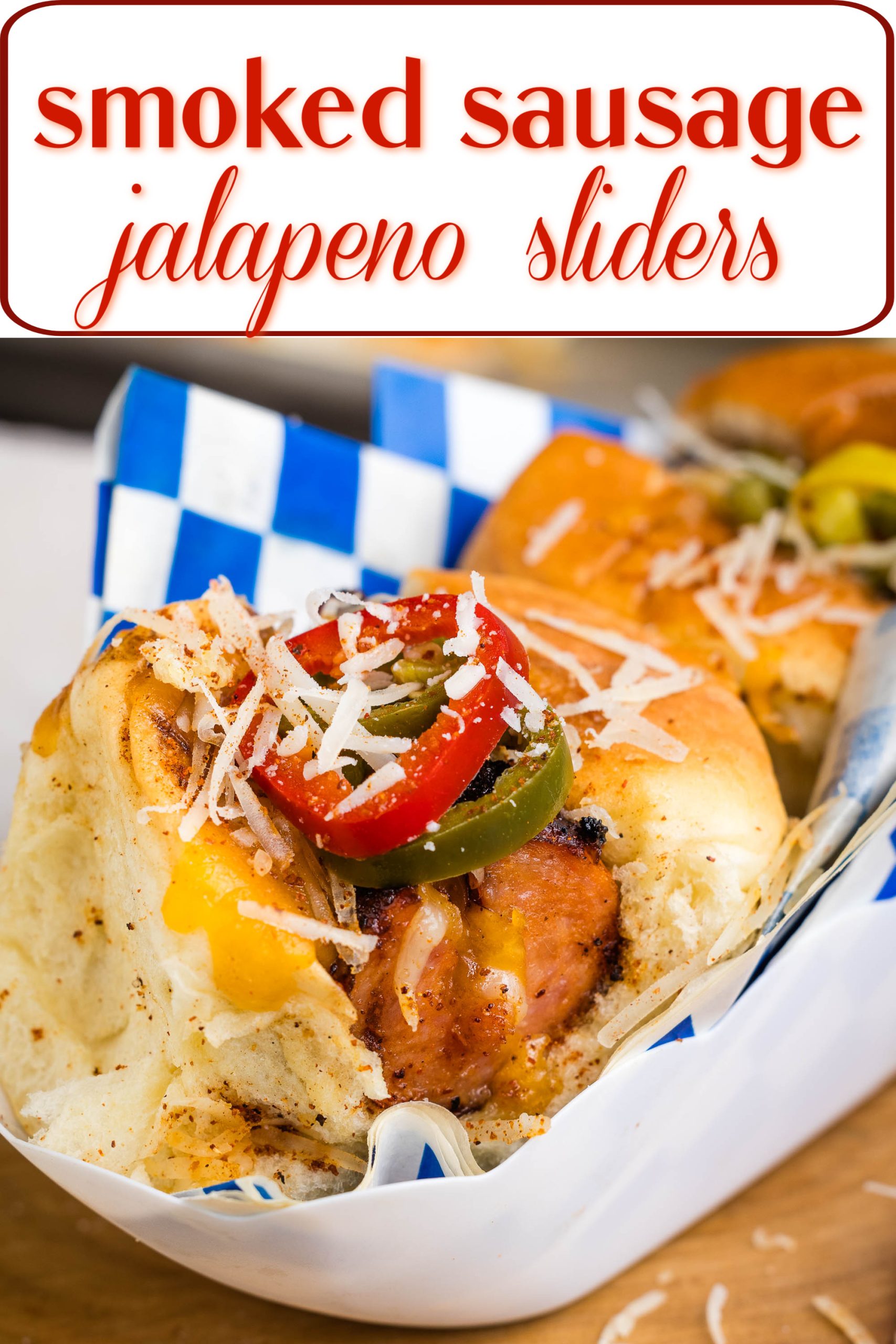 A tray containing smoked sausage sliders topped with jalapenos, cheese, and seasoning in a blue and white checkered paper wrap. The text above reads "smoked sausage jalapeno sliders.