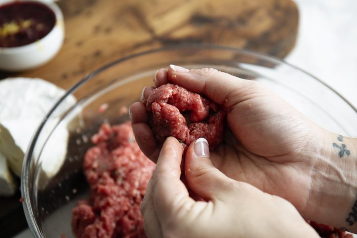 Hands shaping raw ground meat in a glass bowl, preparing for cooking.