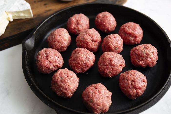 Raw Brie Cheese Stuffed Meatballs arranged in a black skillet on a white surface.