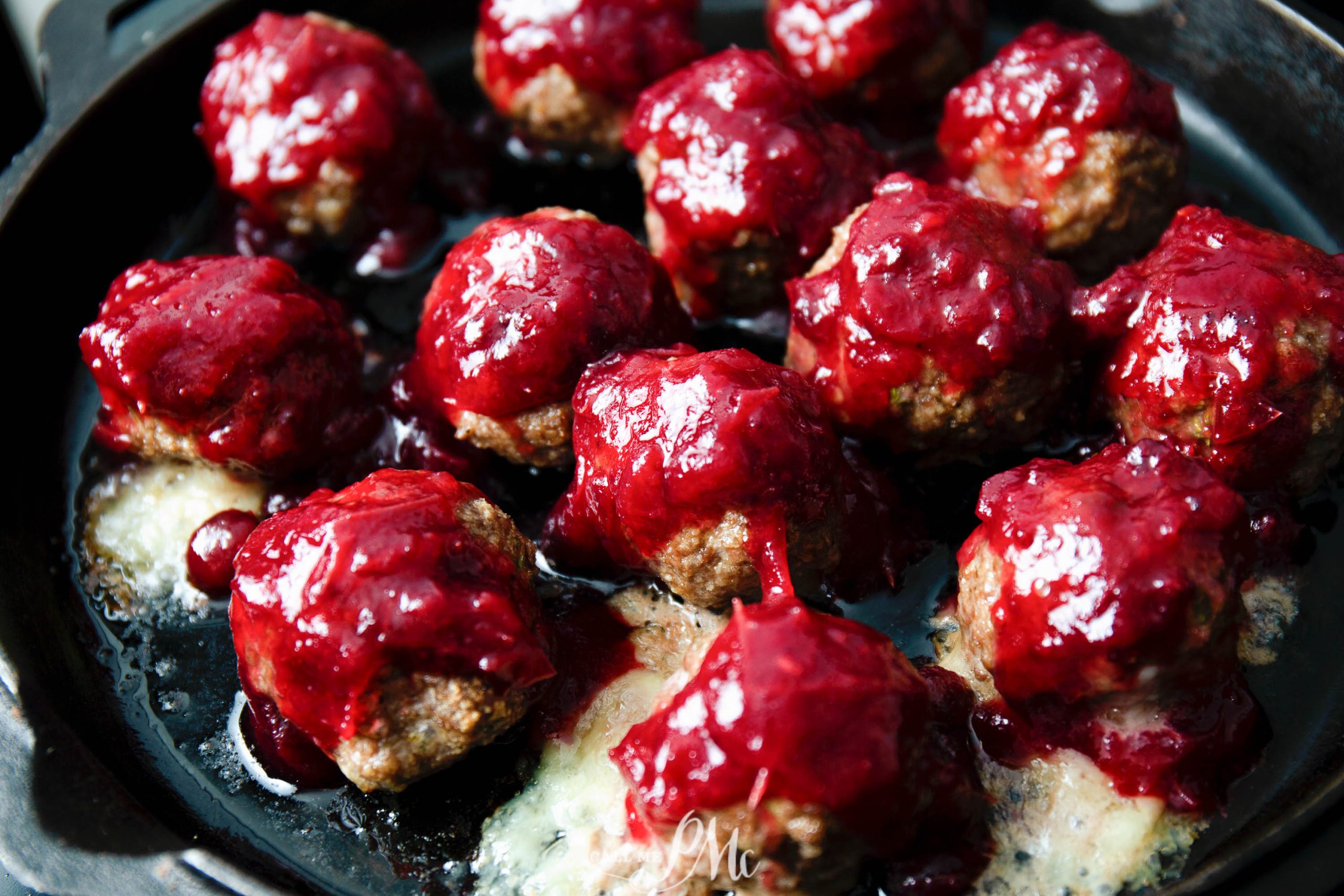 Brie cheese stuffed meatballs coated with a red sauce, arranged beautifully in a black pan.