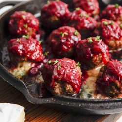 Meatballs topped with sauce and herbs in a cast iron skillet on a wooden surface.