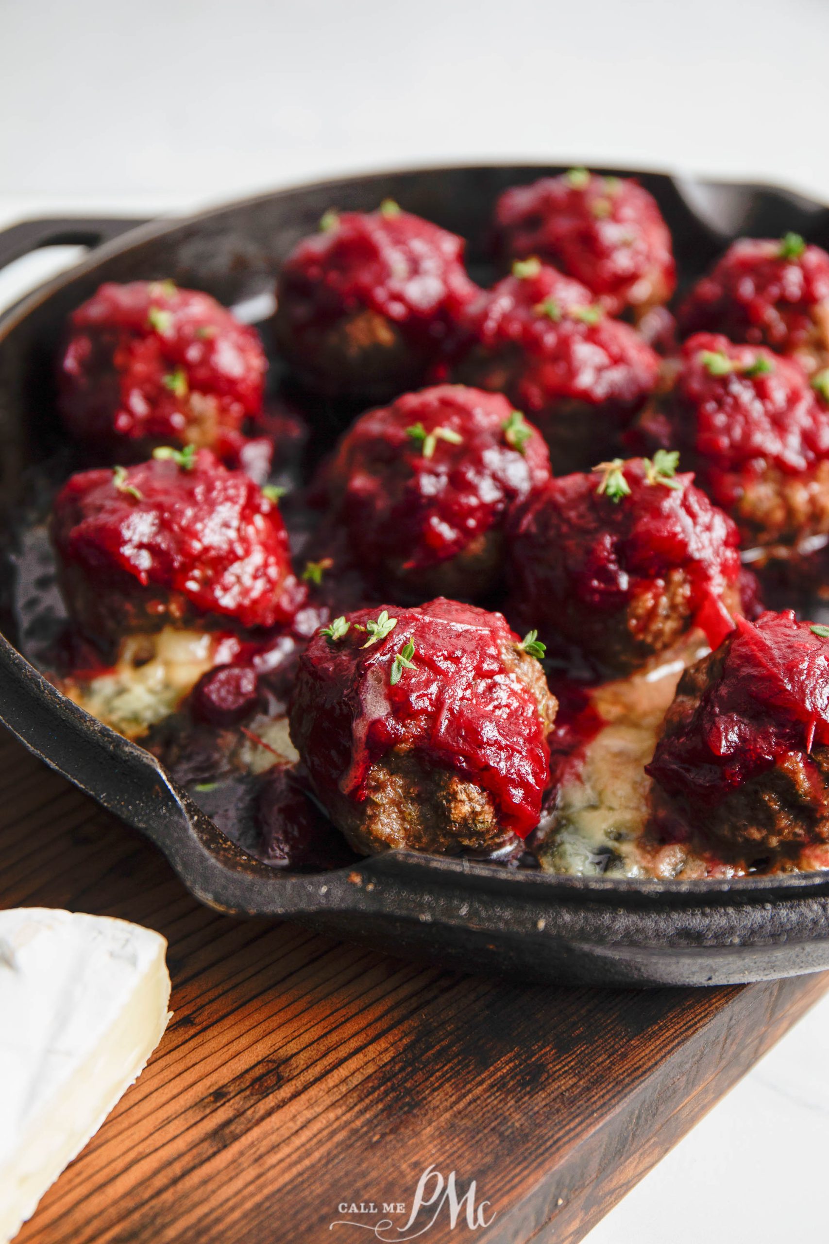 Meatballs topped with sauce and herbs in a cast iron skillet on a wooden surface.