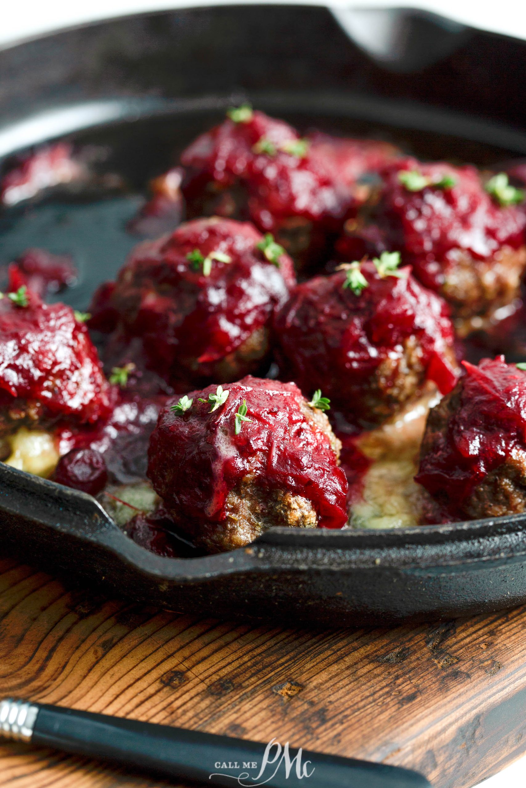 Brie Cheese Stuffed Meatballs covered in a red sauce are arranged in a black cast iron pan, garnished with small green herbs.