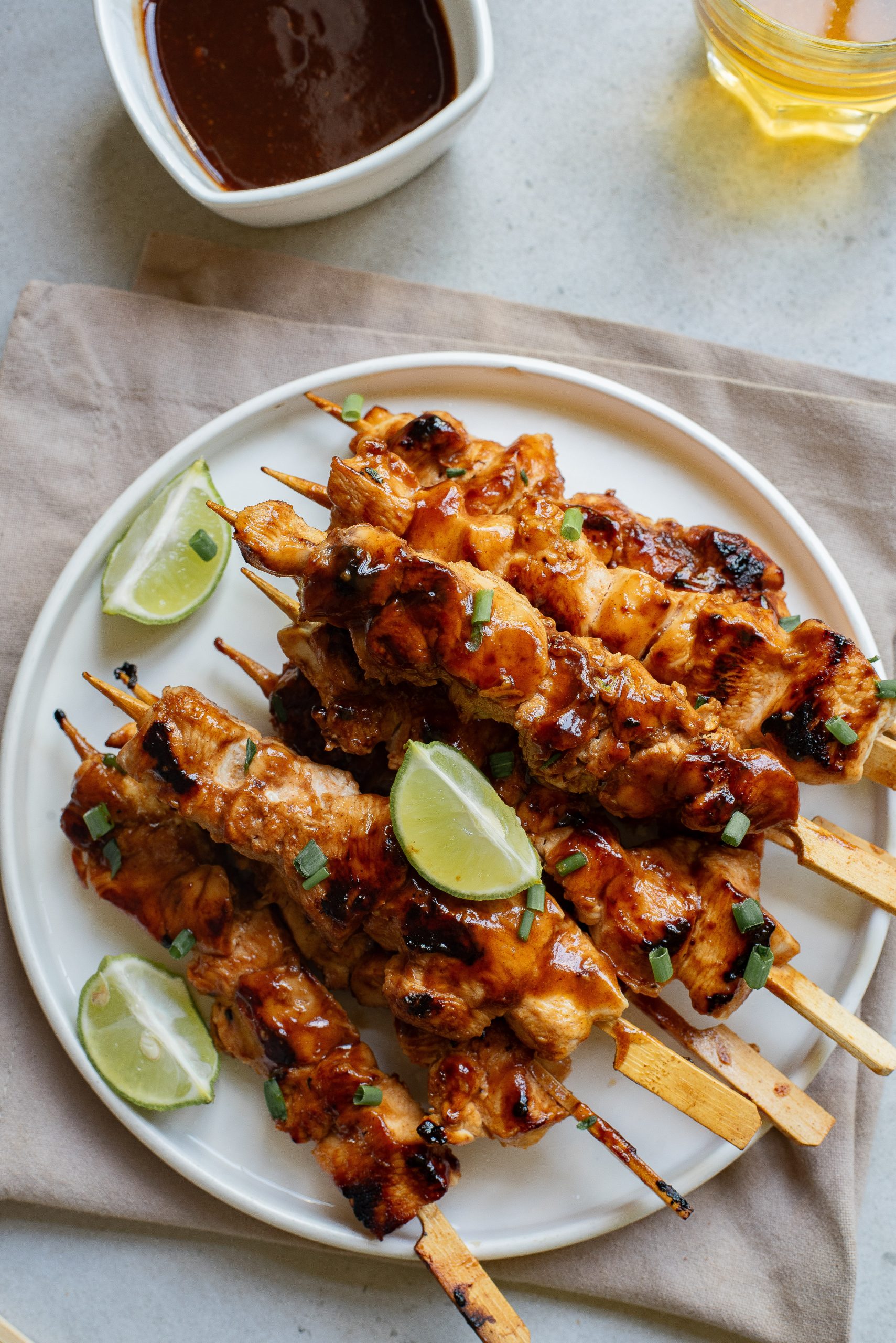 A plate of grilled chicken skewers garnished with lime wedges and herbs, accompanied by a bowl of dipping sauce.