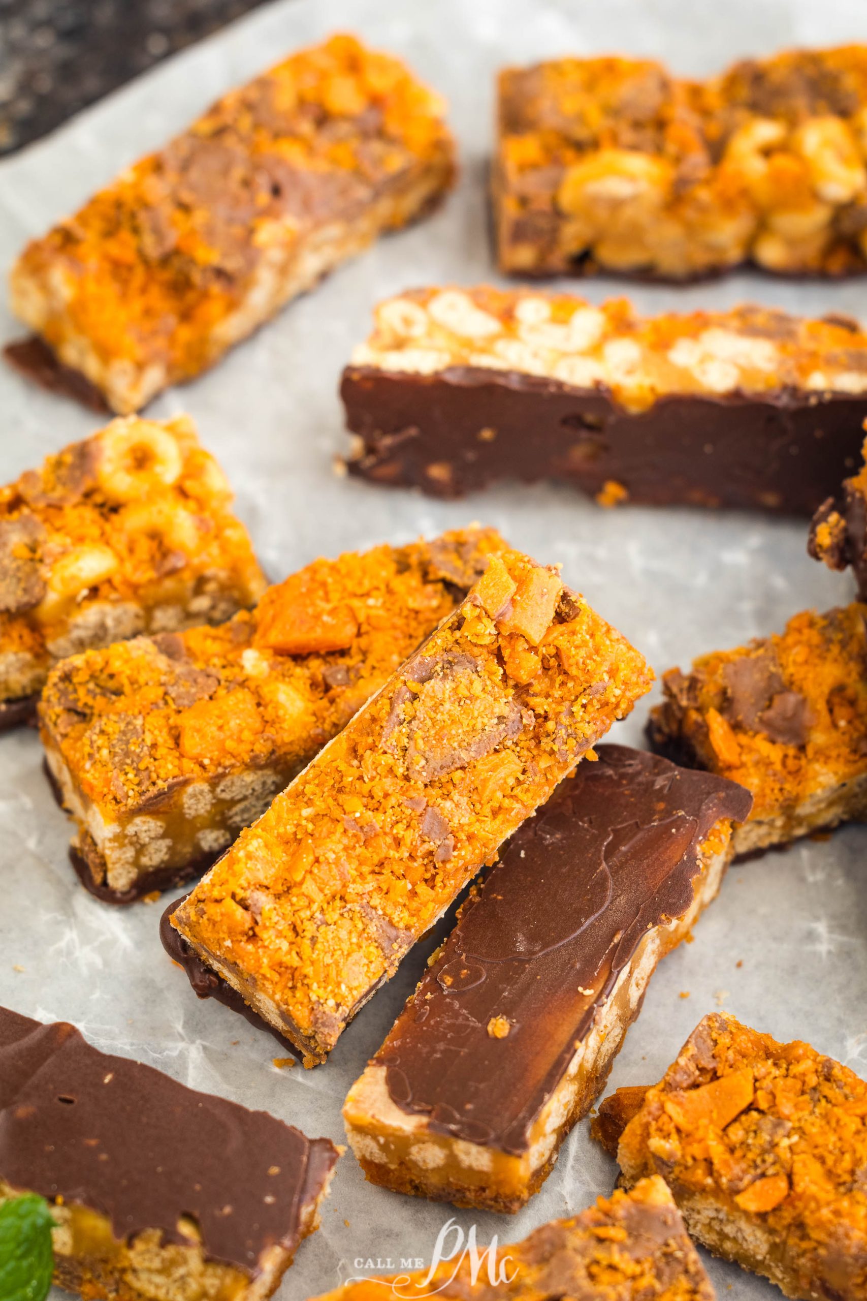 Assorted homemade chocolate and peanut butter bars with crunchy toppings arranged on a parchment-lined surface.