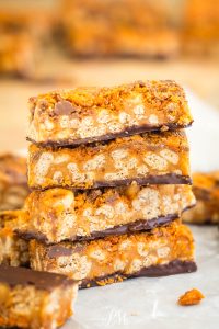 Stack of four caramel and chocolate cereal bars with a crispy texture, showing a layered, crunchy interior on a parchment-lined surface.