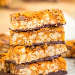 Stack of four caramel and chocolate cereal bars with a crispy texture, showing a layered, crunchy interior on a parchment-lined surface.