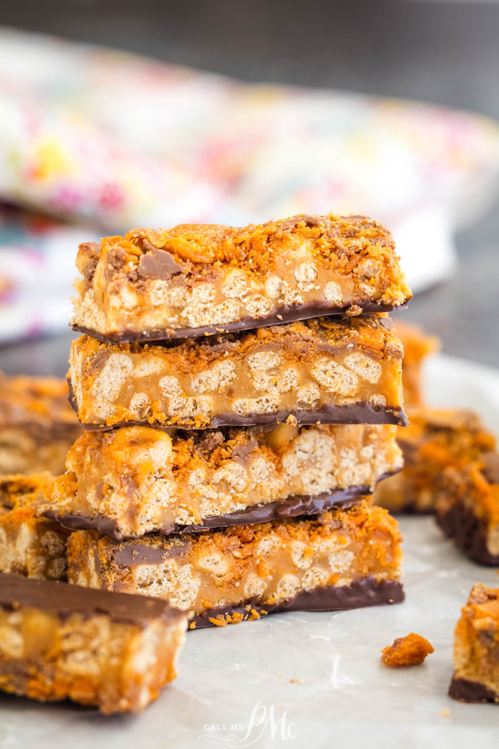 Stack of chocolate and crispy rice cereal bars on a white surface with a blurred floral cloth in the background.