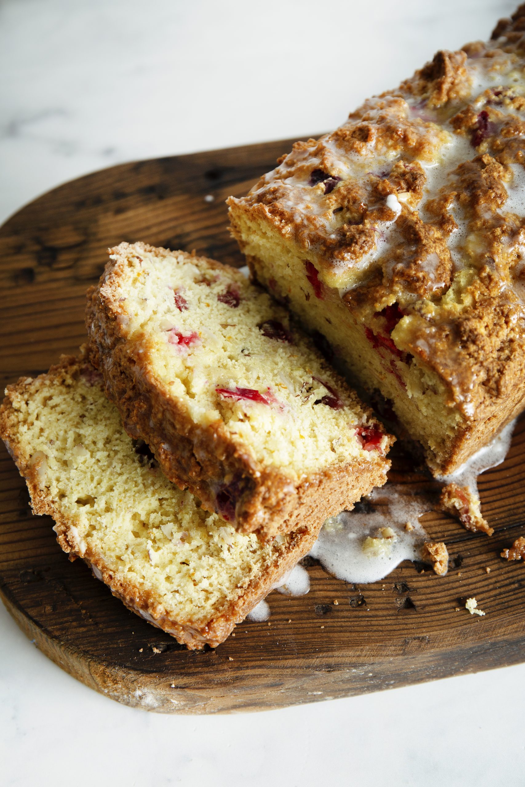 Sliced loaf of Christmas Cranberry Bread with icing on a wooden cutting board.