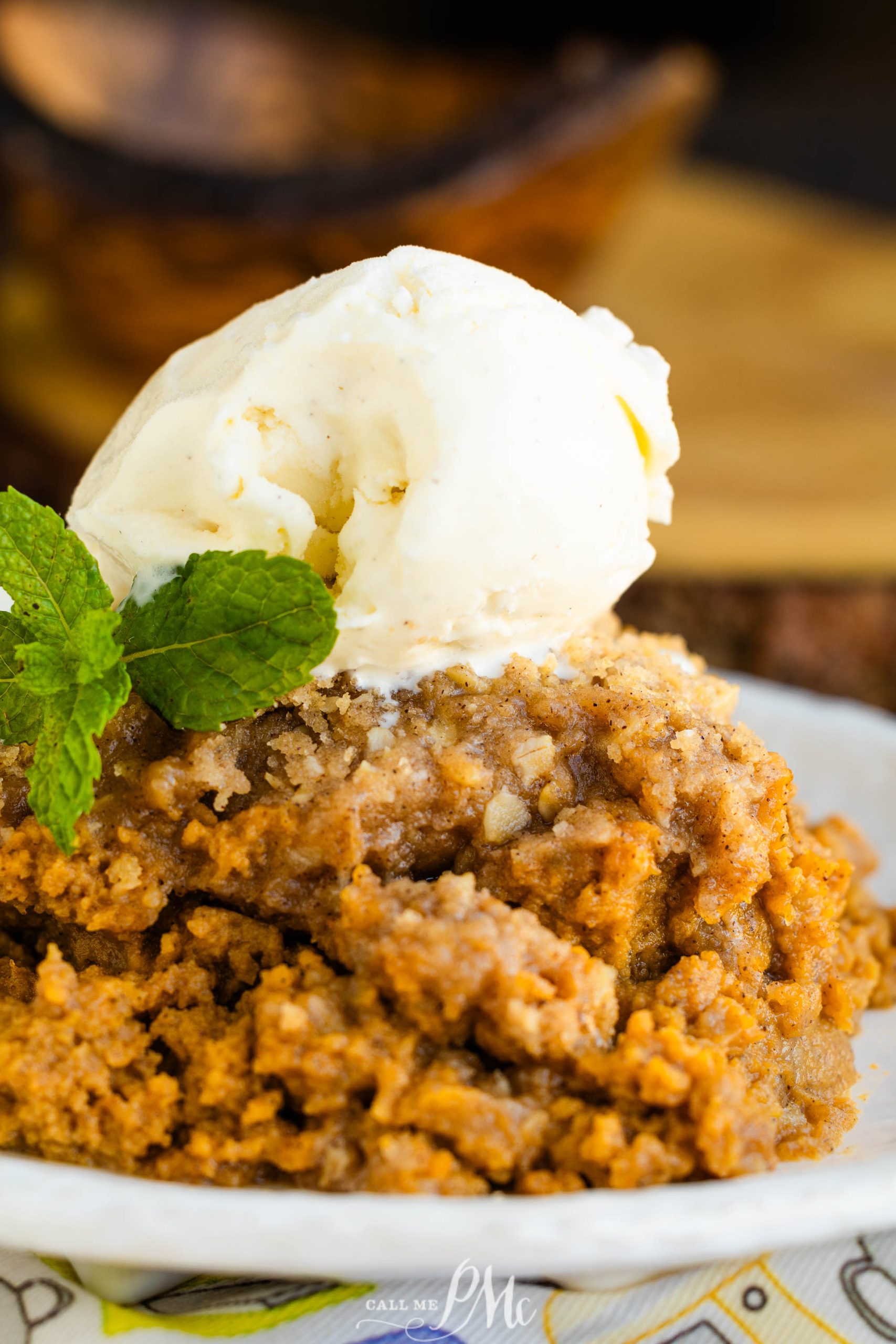 A dessert featuring a serving of pumpkin cobbler topped with a scoop of vanilla ice cream and a sprig of mint.