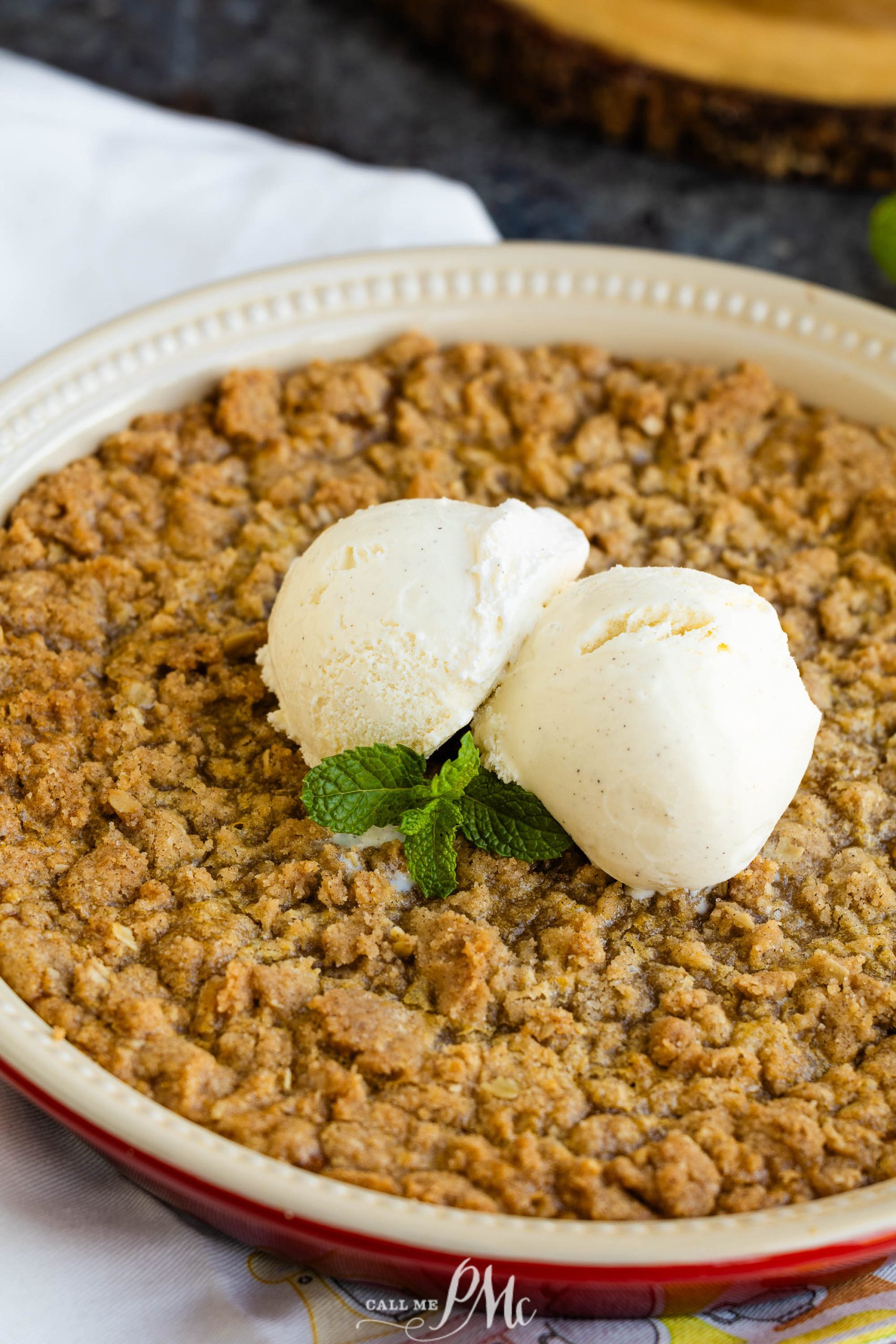 A pie with a crumbly topping, garnished with two scoops of vanilla ice cream and a sprig of mint.