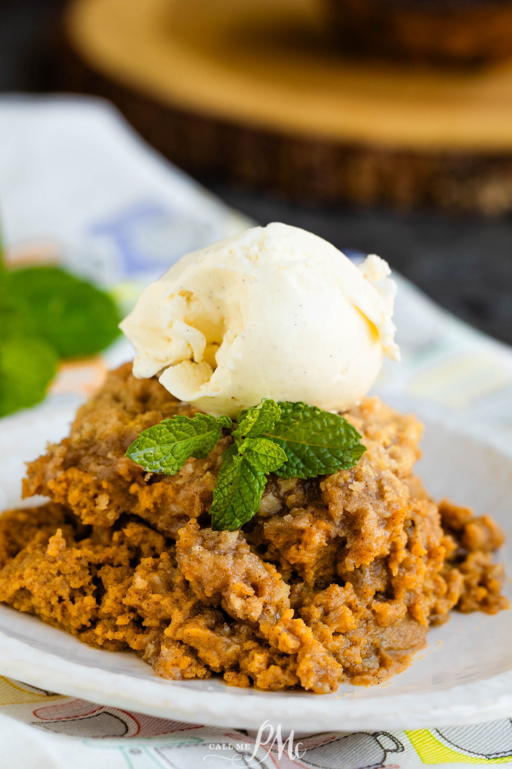 A slice of dessert with a scoop of vanilla ice cream on top, garnished with mint leaves, served on a white plate.