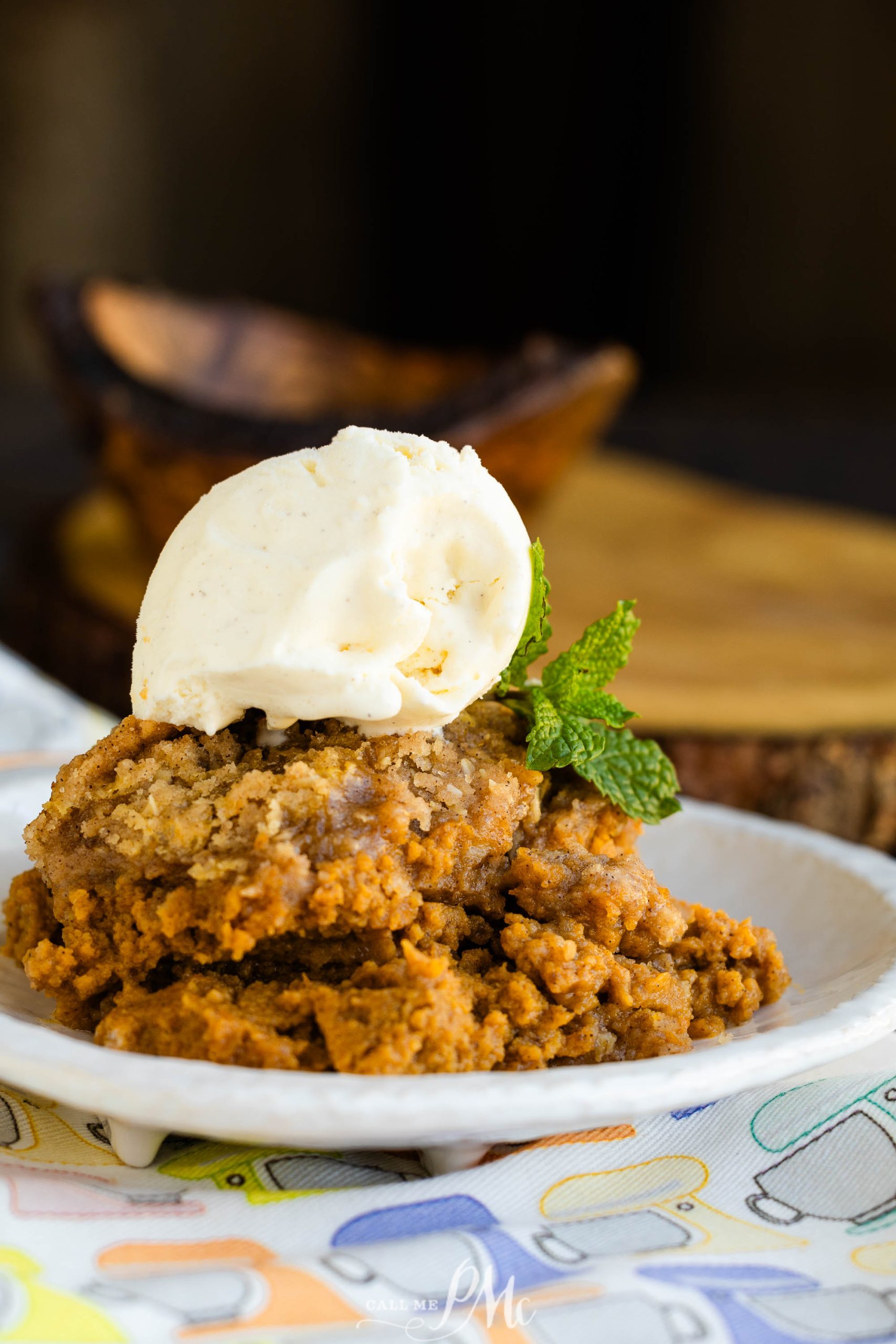 A dessert plate with slices of crumbly pumpkin cobbler topped with a scoop of vanilla ice cream and a mint garnish.