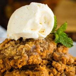 A scoop of vanilla ice cream atop a serving of spiced dessert with a mint garnish on a plate.