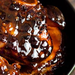 Close-up of a glazed, cooked ham with a shiny, caramelized surface in a black dish, enriched with a maple brown sugar glaze.