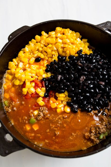 A pot filled with corn, black beans, chopped tomatoes, ground meat, and a brown broth.