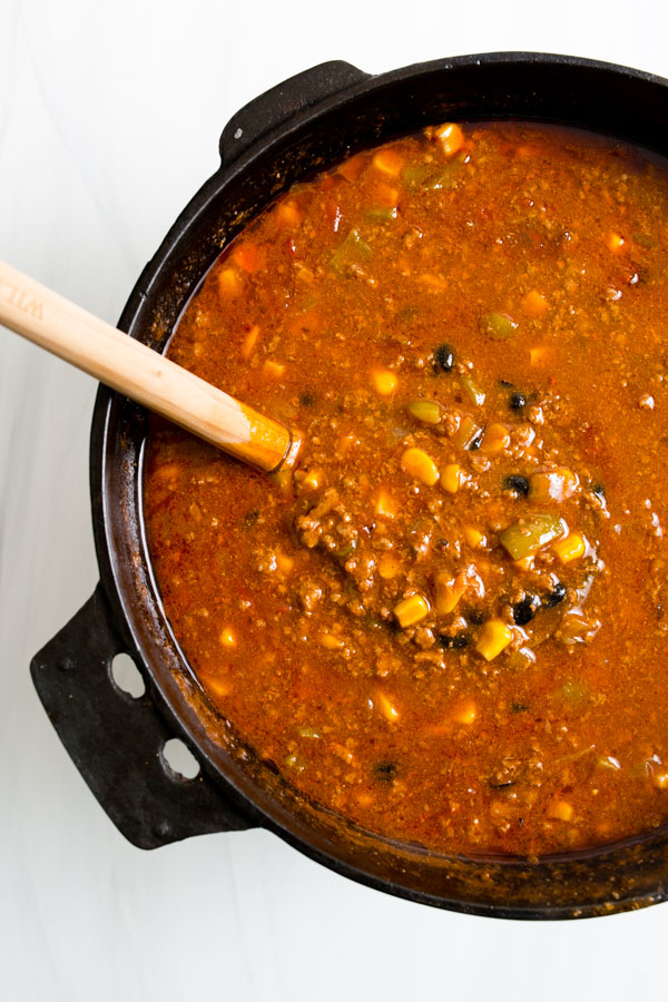 A pot of hearty chili with visible ingredients like corn and beans, and a wooden spoon resting on the side.