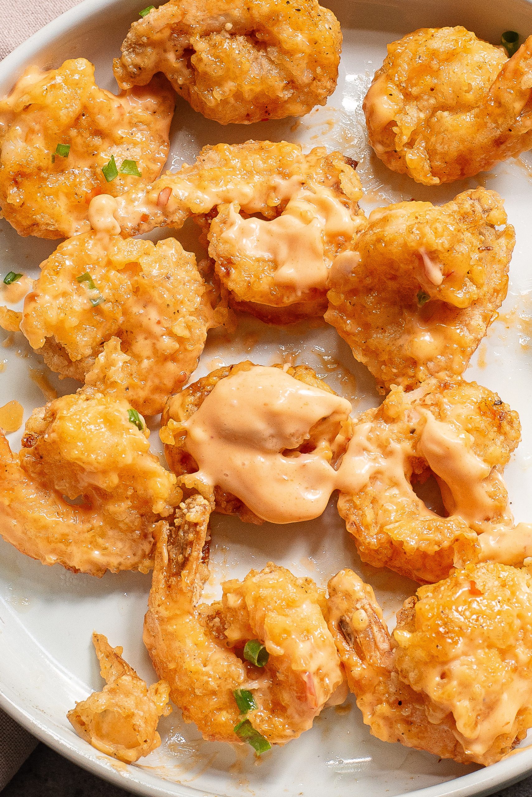 A plate of fried shrimp drizzled with creamy sauce, garnished with green onions, on a white dish.