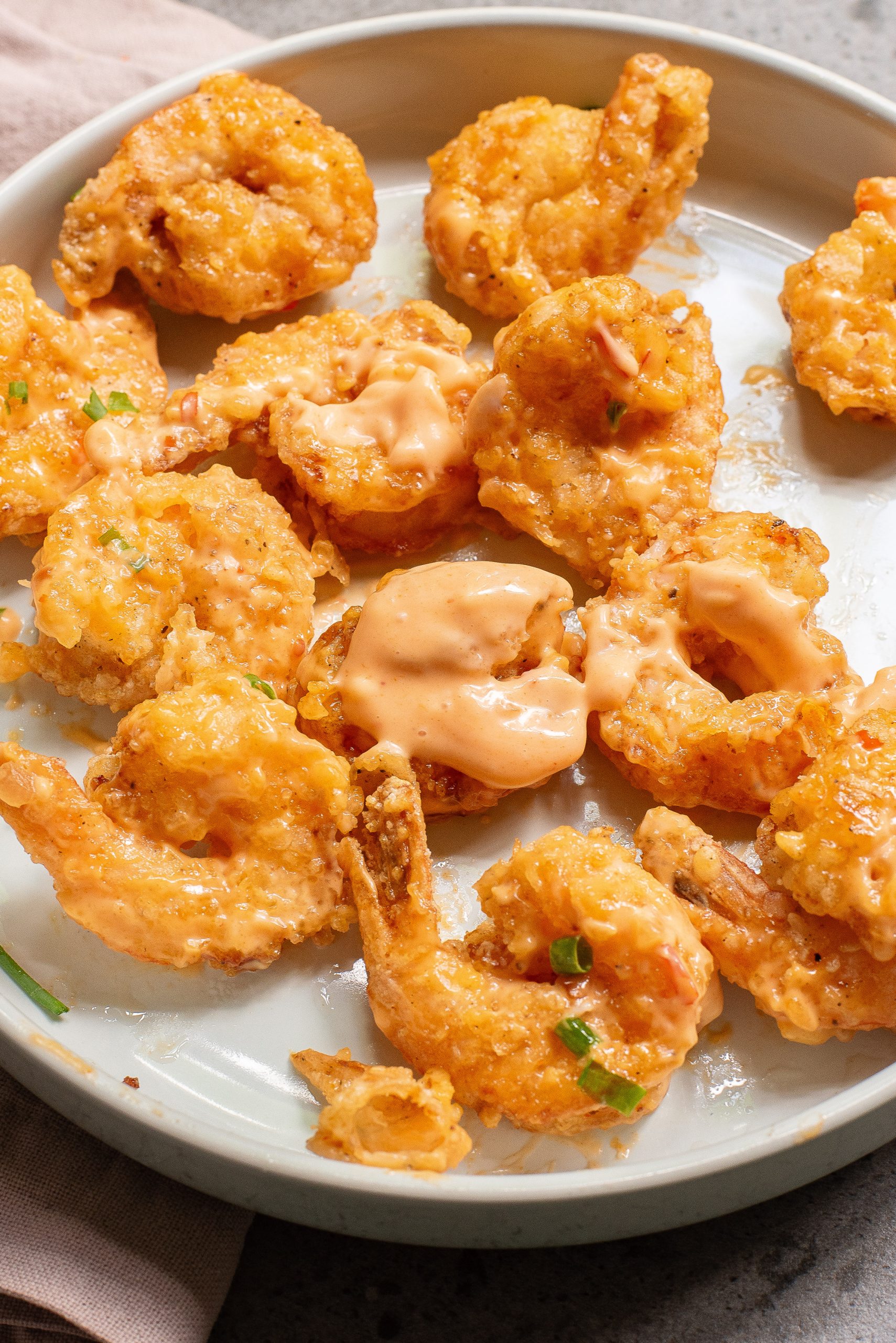 Plate of fried shrimp drizzled with a creamy orange sauce, garnished with chopped green onions.