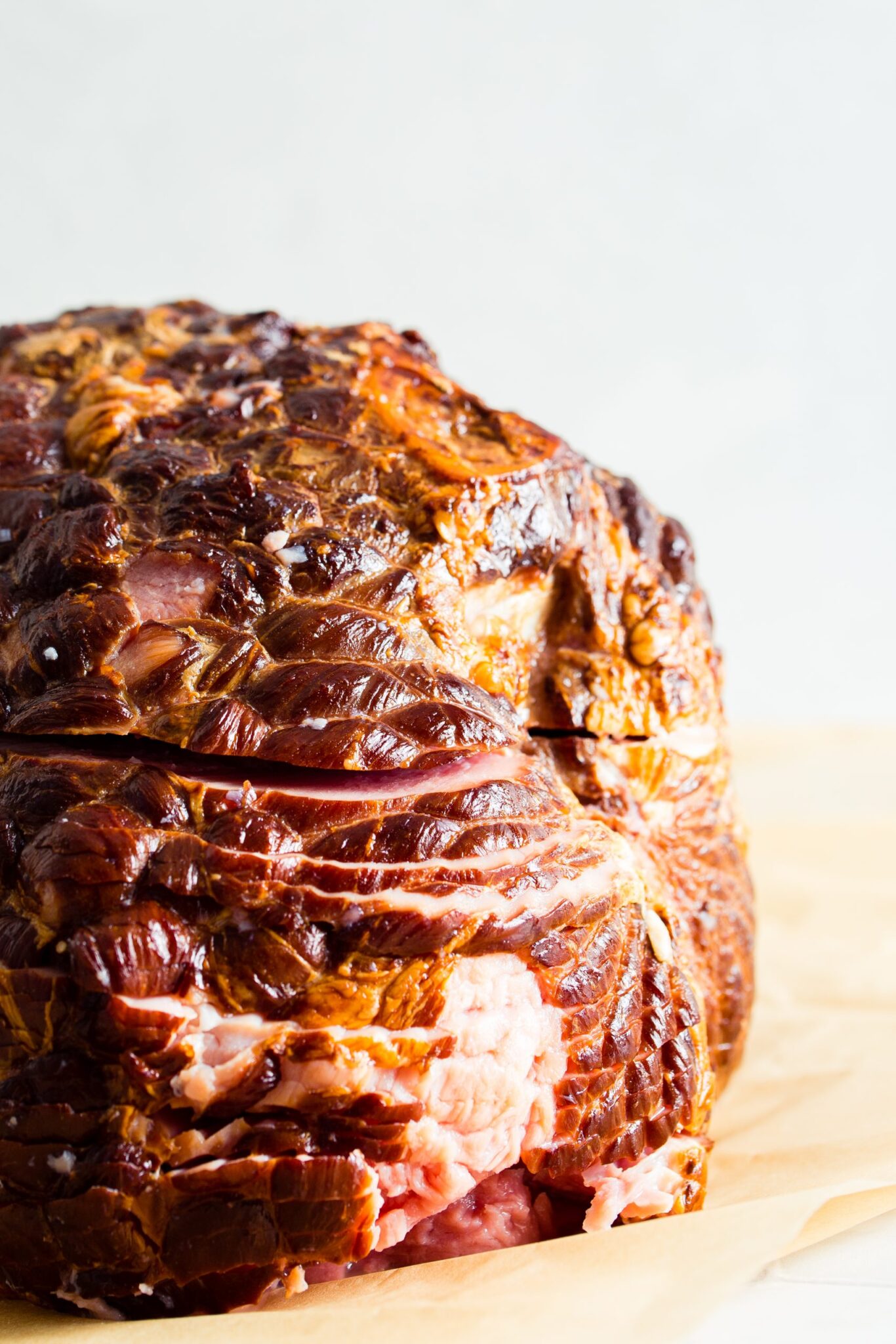 A close-up of a cooked, brown, glazed ham resting on a sheet of parchment paper.