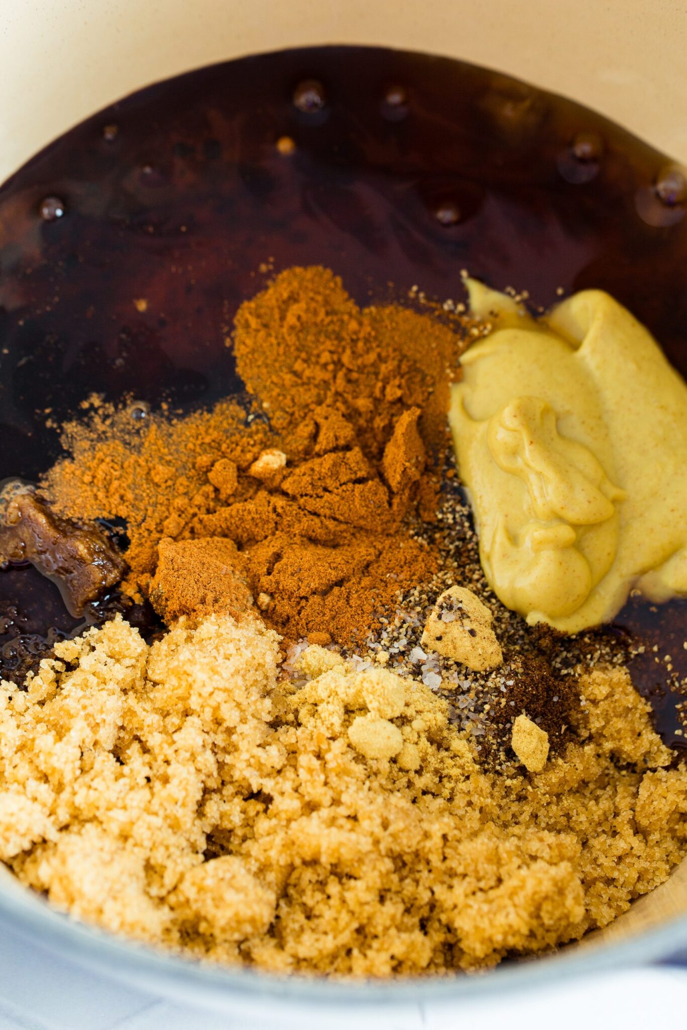 A mixture of brown sugar, mustard, spices, and liquid ingredients in a bowl.