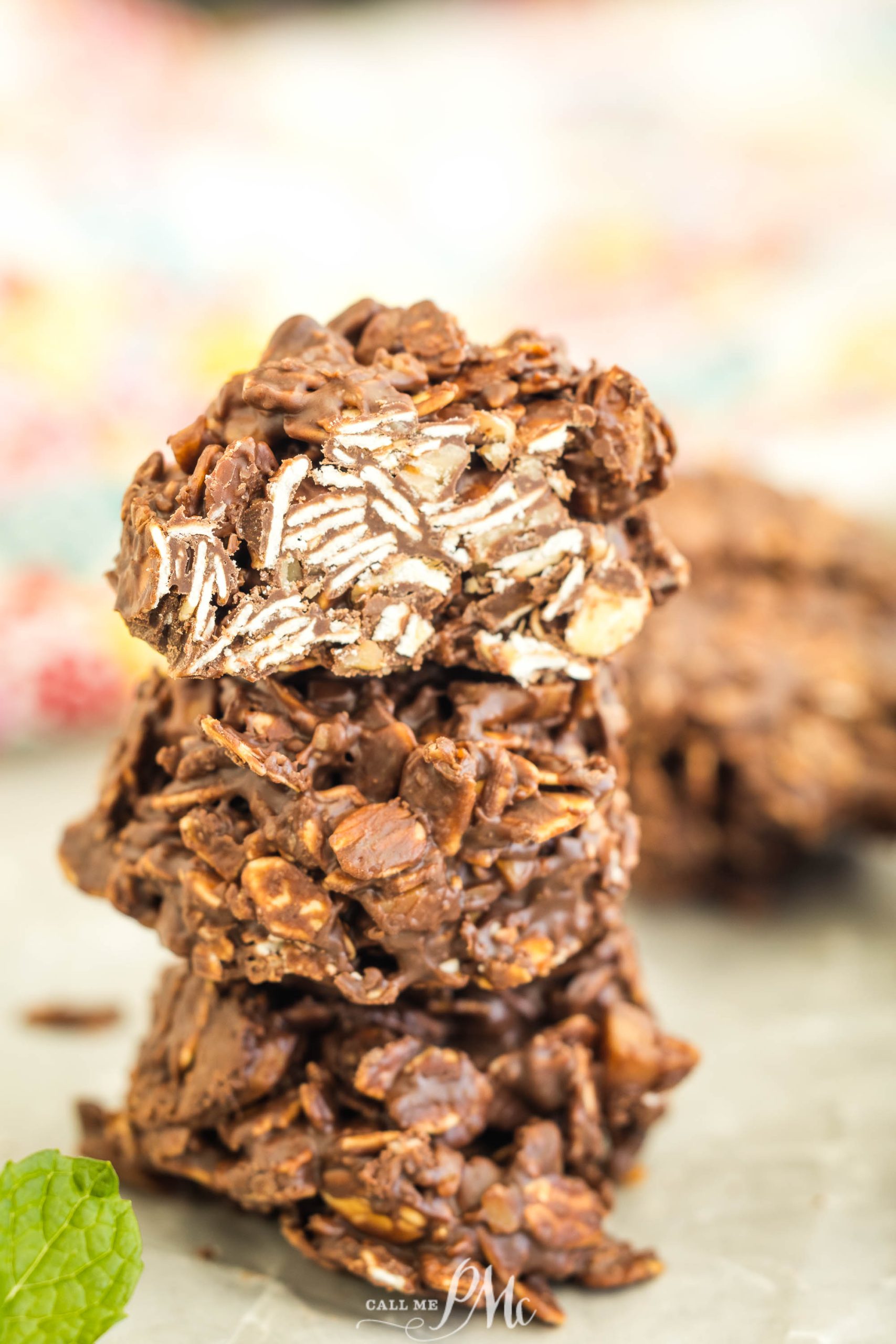 A stack of three chocolate oat cookies with a blurred background and a sprig of mint nearby.