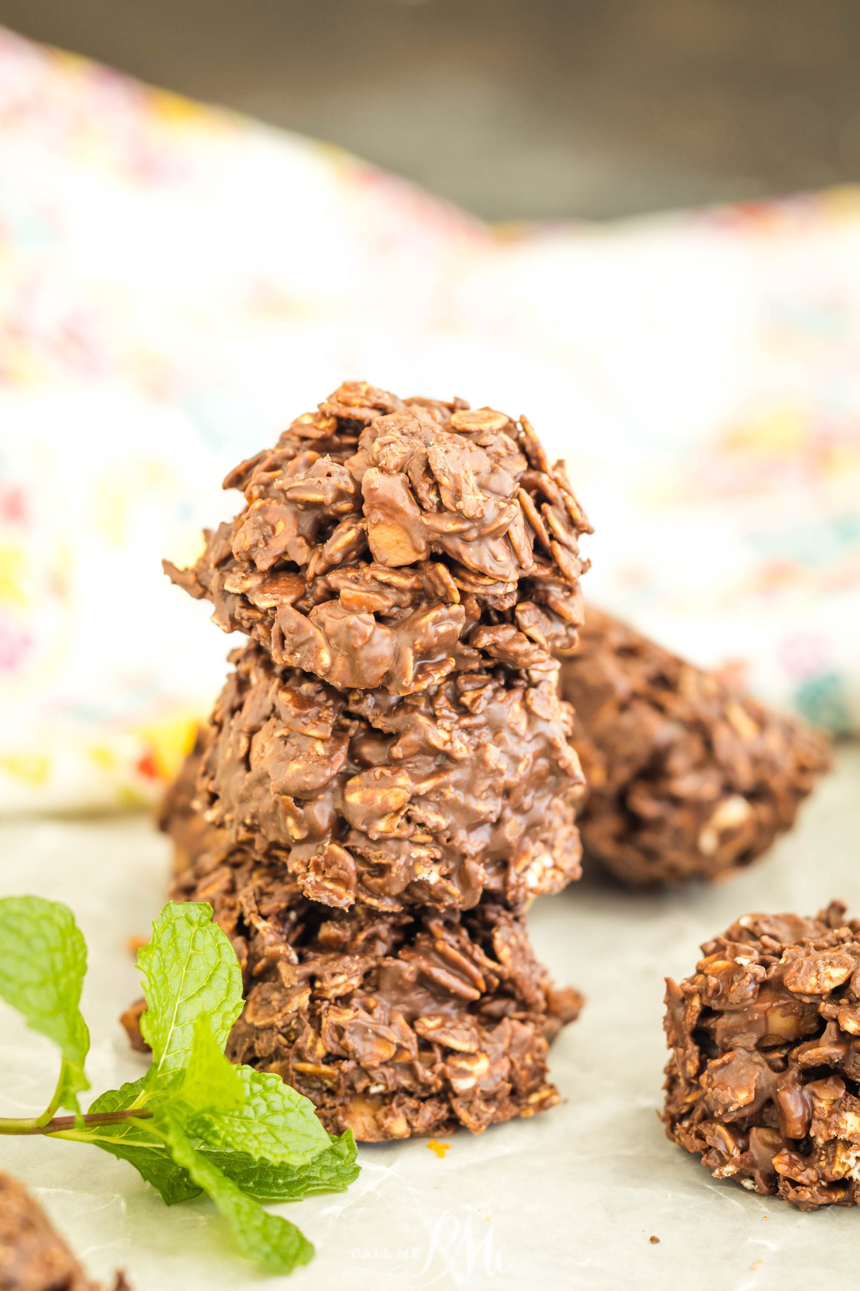 Chocolate oat clusters with a glossy texture are stacked on parchment paper, accompanied by a sprig of fresh mint.